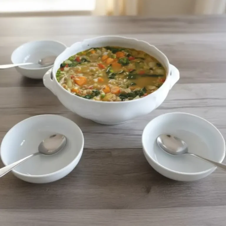 Bol de soupe aux légumes avec orge, servi sur une table avec deux petites assiettes et cuillères.