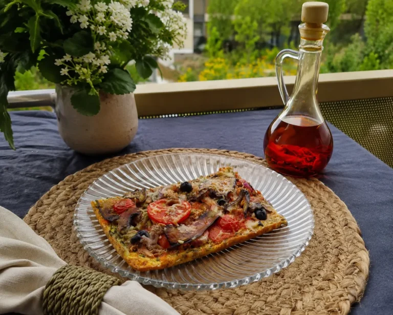 Part de pizza végétale vide-frigo aux courgettes, aubergines, tomates et mozzarella servie dans une assiette blanche en extérieur.
