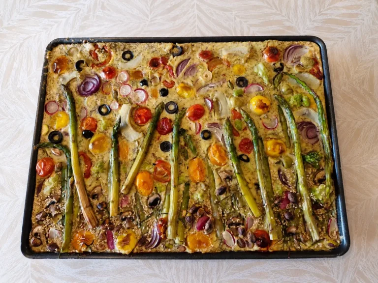 Tableau végétal à la farine de pois chiches garni d’asperges, tomates cerises, radis, olives et légumes de saison, cuit au four.