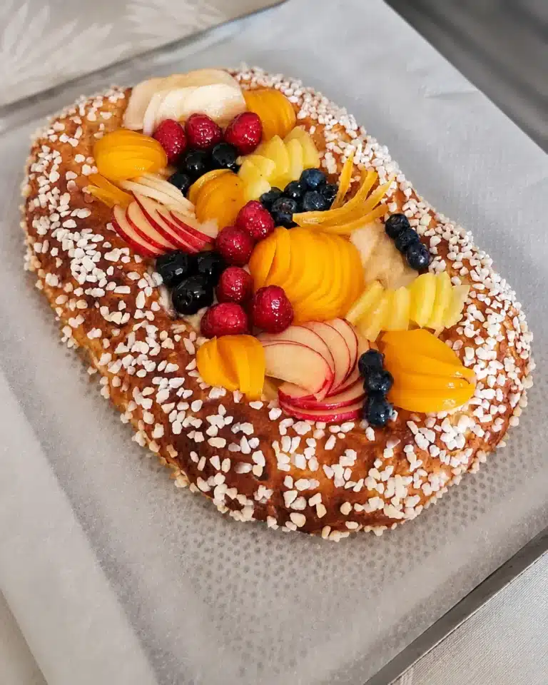 Fougasse catalane aux fruits, brioche moelleuse garnie de crème catalane et de fruits colorés, bordée de sucre en grains.